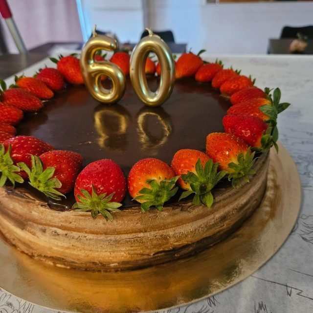 Tarta de chocolate con corona de fresas y el número 60 en velas doradas.