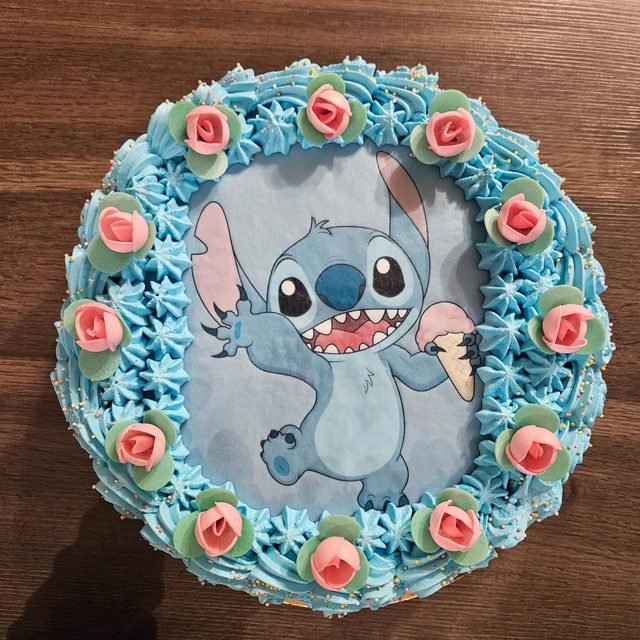 Tarta de cumpleaños con nata azul, rosas de azúcar y una lámina comestible de un personaje de dibujos.