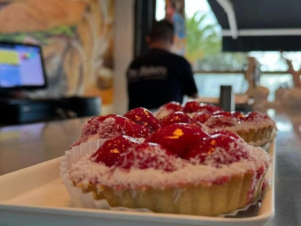 Vista desde el mostrador: una tarta de fresa en primer plano y el local con la luz de la calle al fondo.