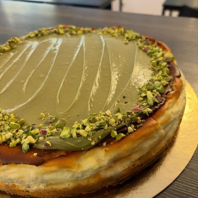 Tarta de queso de pistacho entera, con el borde cubierto de pistacho picado.